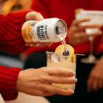 Close-up of a Christmas cocktail being poured into a glass with warm Texas holiday lights in the background.
