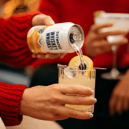 Close-up of a Christmas cocktail being poured into a glass with warm Texas holiday lights in the background.