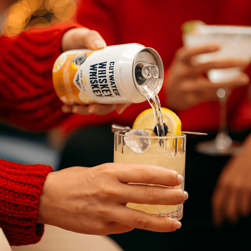 Close-up of a Christmas cocktail being poured into a glass with warm Texas holiday lights in the background.
