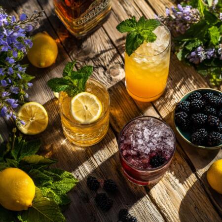 Spring whiskey cocktails with fresh lemon, mint garnish and ice served on rustic Texas patio table