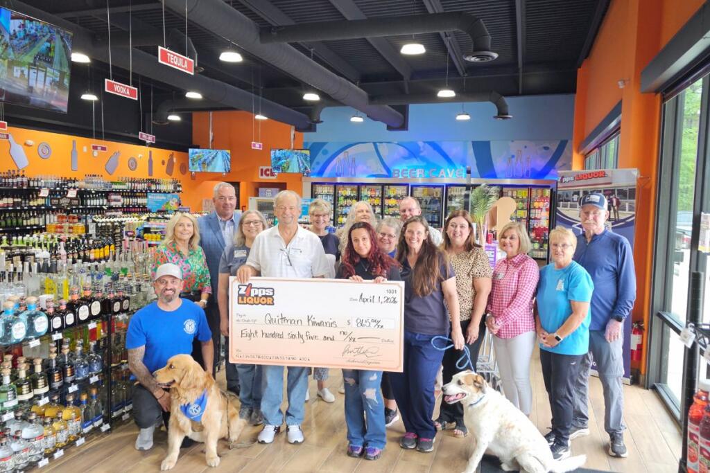 Zipps Liquor Quitman staff and Quitman-Lake Fork Kiwanis Club members holding $865 donation check inside the store with spirits shelves beer cave and tequila section visible in background April 2026